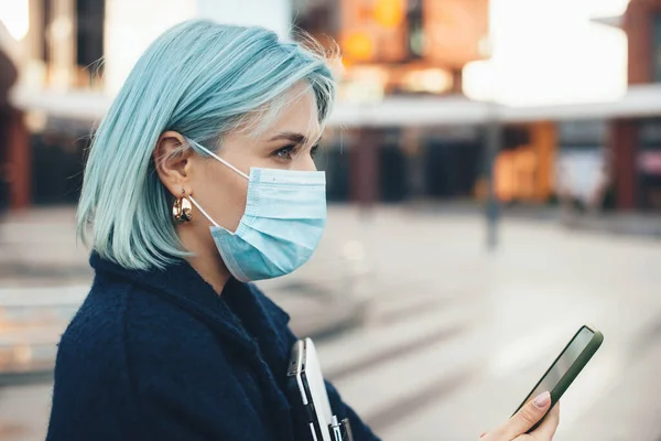 Antreprenor caucazian superb cu păr albastru pozând cu gadget-uri moderne în timp ce poartă o mască anti-gripă — Fotografie, imagine de stoc