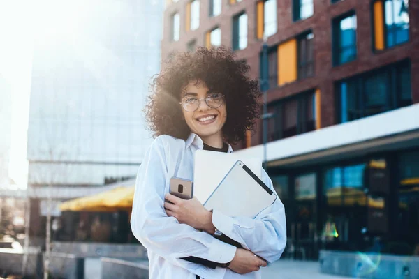 Curly cabelos caucasianos mulher olhando para a câmera enquanto posando com seu telefone e computador fora — Fotografia de Stock