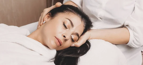 Hoofd massage procedure met een brunette Kaukasische dame liggend op de bank in de spa salon — Stockfoto