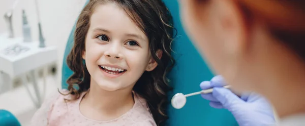 Niña rizada mirando y sonriendo al dentista después de un chequeo —  Fotos de Stock