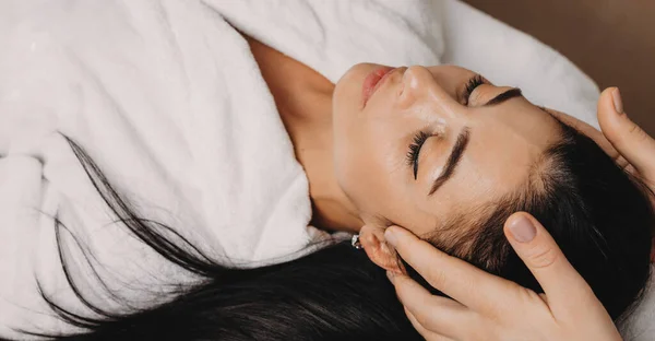 Mulher branca deitada no sofá enquanto faz uma sessão de massagem na cabeça no salão de spa — Fotografia de Stock