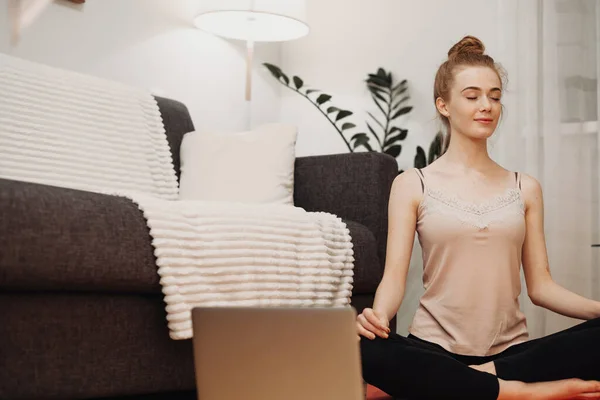 Mujer caucásica con cabello rojo y pecas meditando y haciendo ejercicios de fitness en el suelo mientras usa una computadora — Foto de Stock