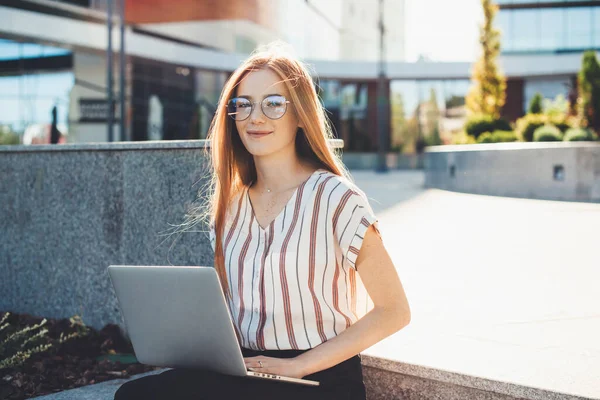 Ingefära kaukasiska affärskvinna med fräknar och glasögon arbetar med en dator utanför — Stockfoto