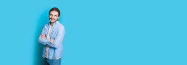 Beyaz adam, uzun saçlı ve sakallı. Mavi duvarda el ele tutuşurken poz veriyor.