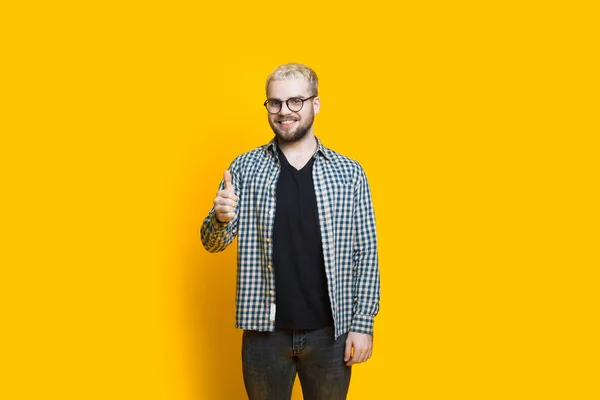 Homem barbudo caucasiano com óculos e cabelo loiro está gesticulando o sinal de aprovação em uma parede amarela — Fotografia de Stock
