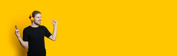 Homem barbudo caucasiano com fones de ouvido e cabelos longos está dançando em uma parede amarela com espaço em branco — Fotografia de Stock