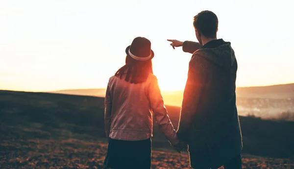 Vit man går hand i hand med sin flickvän på ett fält pekar på den perfekta solnedgången. — Stockfoto