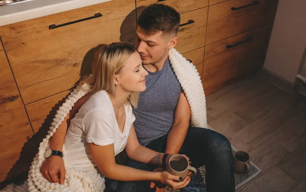 Adorável casal caucasiano sentado no chão na cozinha e beber um chá juntos — Fotografia de Stock