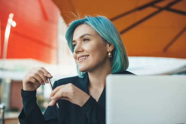Γοητευτική επιχειρηματίας με μπλε μαλλιά κάθεται σε ένα εστιατόριο και εργάζεται με έναν υπολογιστή — Φωτογραφία Αρχείου