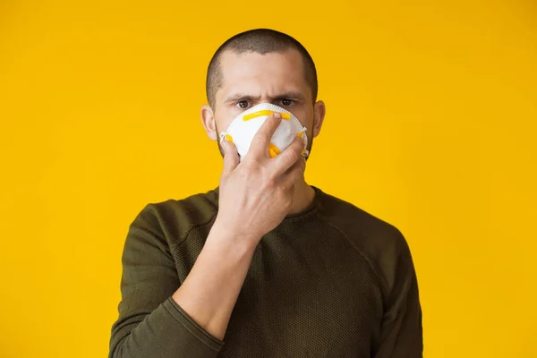 Feche o retrato usando uma máscara protetora em uma parede amarela e olhando para a câmera seriamente — Fotografia de Stock