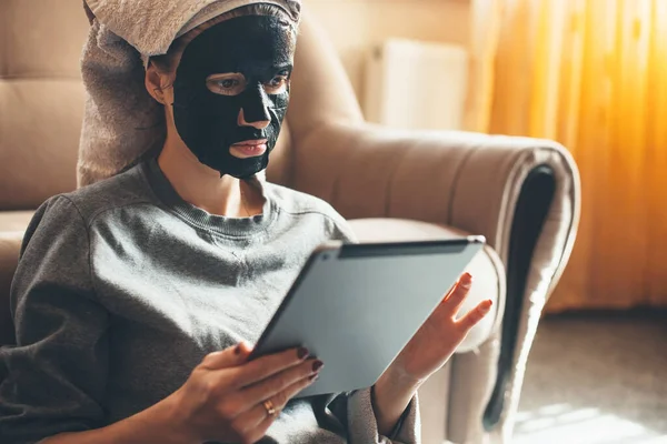 Zblízka portrét bělošky, která doma nosí černou masku a používá tablet na podlaze — Stock fotografie