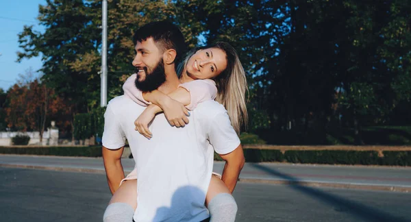 Bearded man in white clothes carrying his girl and smiling outside in the street — Stock Photo, Image