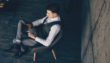 Bir tabletle çalışan ve bir koltukta oturan Kafkasyalı bir adamın üst görünüm portresi
