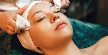 Kafasında havluyla kaplıca koltuğunda uzanan genç bir kadınla baş masajı seansı.