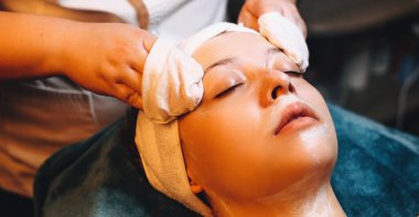 Beyaz kadın spa salonundaki kanepede uzanmış özel kremalı yüz masajı yaptırıyor.