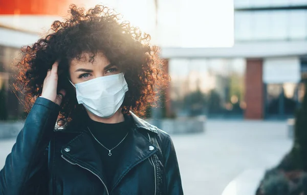 Ung kaukasisk kvinde med krøllet hår og sort læderjakke bærer beskyttende maske - Stock-foto