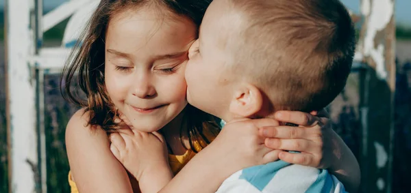 Kafkasyalı sarışın bir çocuğun yakın portresi ve kız kardeşi onu öpüyor ve gün batımına karşı sarılıyor. — Stok fotoğraf