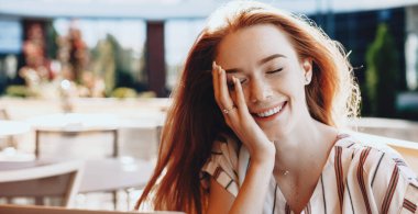 Kafeteryada vakit geçirirken çilli, gülümseyen ve yüzüne dokunan kızıl kadın.