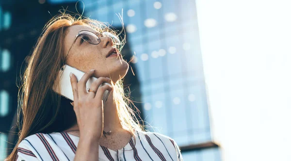 Rothaarige kaukasische Geschäftsfrau mit Sommersprossen und Brille schaut auf und telefoniert an einem windigen, sonnigen Tag — Stockfoto