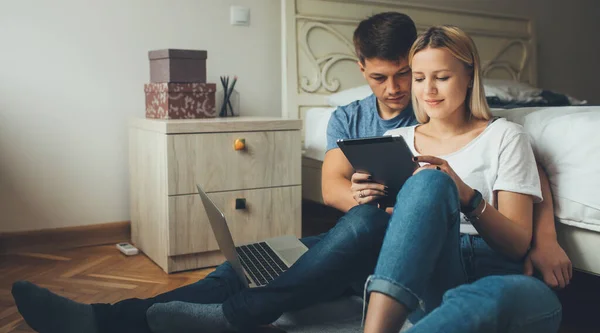 Молода біла пара щось планує, використовуючи планшет і блокнот на підлозі в спальні — стокове фото