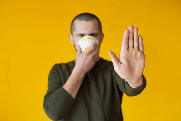 Homem caucasiano alertado usando uma máscara estéril e gesticulando o sinal de parada em um fundo de estúdio amarelo — Fotografia de Stock