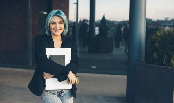 Bella donna con i capelli blu e telefono in posa di fronte a un edificio con occhiali che tengono il computer portatile — Foto Stock