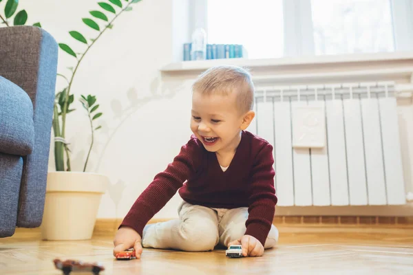 Милый мальчик играет на полу с игрушечными машинами и весело смеется — стоковое фото