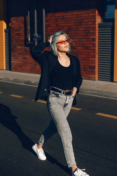 Impresionante mujer de moda con el pelo azul y gafas rojas posando fuera en la calle durante un día soleado — Foto de Stock