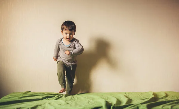 Niño encantador jugando y corriendo en el sofá pasar tiempo solo en el dormitorio —  Fotos de Stock