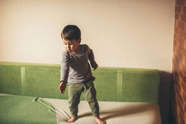Pequeño chico caucásico apuntando al suelo mientras está sentado en el sofá verde —  Fotos de Stock
