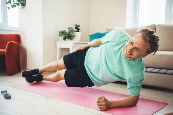 Homem branco loiro sorrindo ao fazer exercícios em um tapete de ioga em casa — Fotografia de Stock