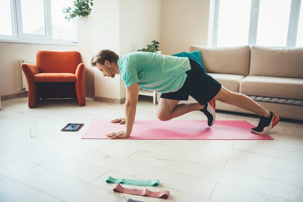 Homem caucasiano fazendo exercícios esportivos em casa enquanto olha para o tablet no chão — Fotografia de Stock
