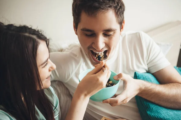 Carino coppia caucasica mangiare cereali a letto mattina presto abbracciare e sorridere insieme — Foto Stock