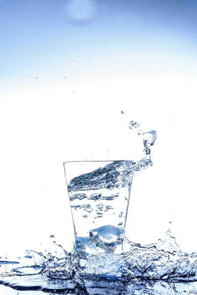 Jég, csepegtető, és fröccsenő tükörképe a pohárban a víz — Stock Fotó