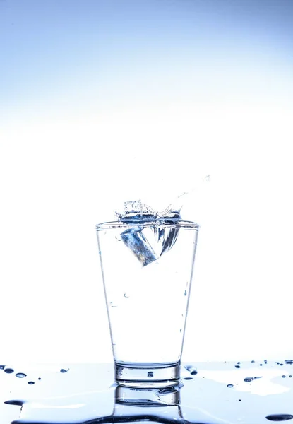 Jég, csepegtető, és fröccsenő tükörképe a pohárban a víz — Stock Fotó