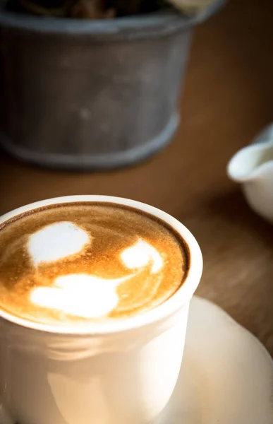 Una taza de café con espuma de leche de San Valentín en el plato blanco y — Foto de Stock
