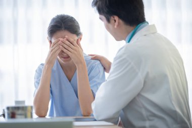Bir doktor, üzgün ve unh ile hasta bir kadına bakar.