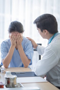 Bir doktor, üzgün ve unh ile hasta bir kadına bakar.