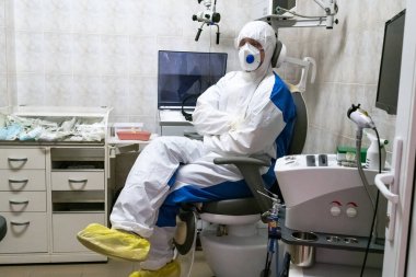 Salgın döneminde koruyucu giysili bir doktor muayene koltuğunda oturuyor. Salgın hastalık konsepti. Seçici odak.