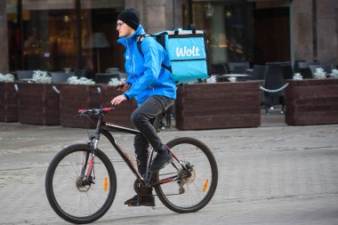 RIGA, LATVIA. 16th October 2019. WOLT company food delivery. Young man on bicycle holds smartphone in hands. clipart