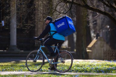 RIGA, LATVIA. 8 Nisan 2020. Seçici odak fotoğrafı. Wolt Şirketi yiyecek dağıtım işçisi Riga City 'de bisiklet sürüyor. Wolt, gıda dağıtım platformuyla tanınan Fin teknoloji şirketidir..