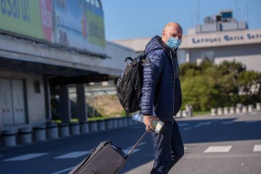 RIGA, LATVIA. 7 Mayıs 2020. Koruyucu kostümler giyen otobüs çalışanları Riga Uluslararası Havaalanı 'na vardıklarında yolcuları bekleyen koruyucu maskelerle karşılaşıyorlar..