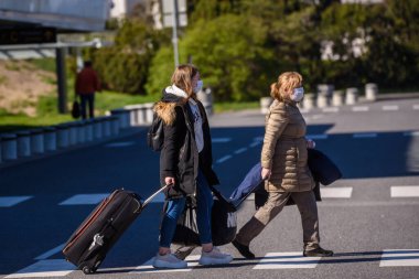 RIGA, LATVIA. 7 Mayıs 2020. Koruyucu kostümler giyen otobüs çalışanları Riga Uluslararası Havaalanı 'na vardıklarında yolcuları bekleyen koruyucu maskelerle karşılaşıyorlar..