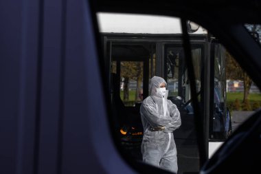 RIGA, LATVIA. 7 Mayıs 2020. Koruyucu kostümler giyen otobüs çalışanları Riga Uluslararası Havaalanı 'na vardıklarında yolcuları bekleyen koruyucu maskelerle karşılaşıyorlar..