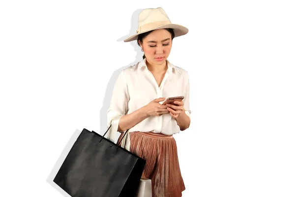 एक स्मार्टफ़ोन देखने और शॉपिंग बैग पकड़ने के लिए युवा एशियाई महिला — स्टॉक फ़ोटो, इमेज