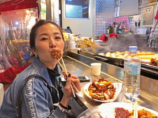 Молодая женщина ест хрустящие корейские жареные куриные уличные блюда в S Стоковое Изображение