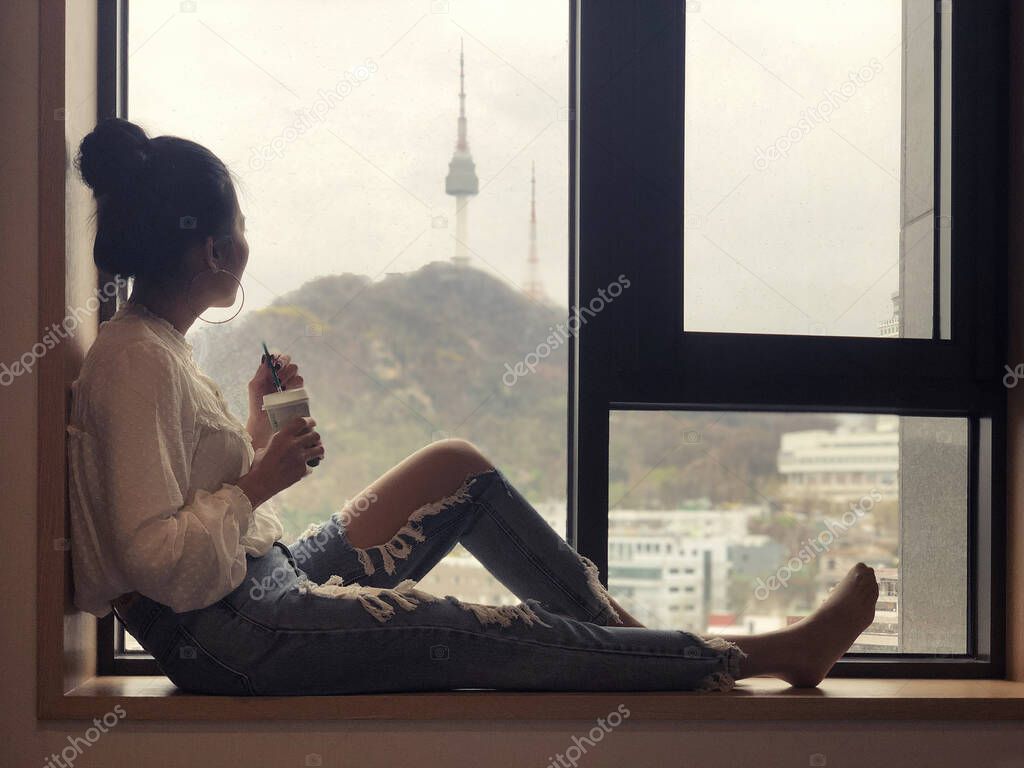 Young woman drinking coffee and looking out the window to see th