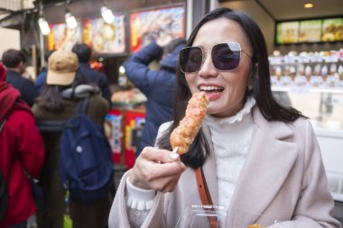 Yakitori yiyen genç turist kadın, Japonya 'daki Arashiyama bambu ormanının meşhur sokak yemeği olarak ızgara yapılmış tavuk.