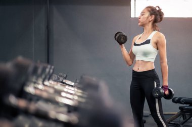 Spor salonunda dambılları kaldıran sağlıklı genç bir kadın.