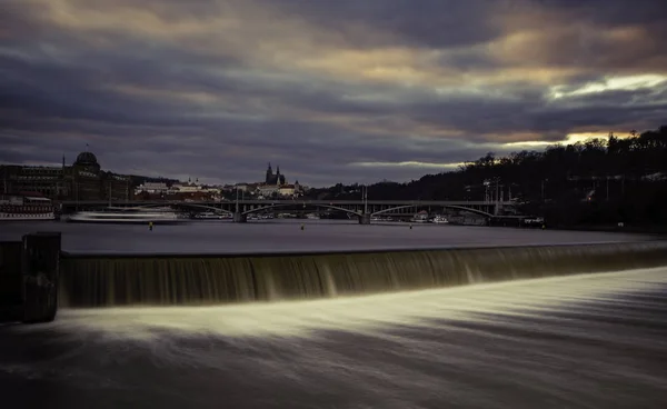 ヴルタヴァ川と橋手前の上の都市と堰とプラハ城珍しい夜表示 夕日と街をカラフルな雲 — ストック写真